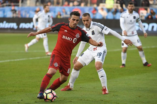 Luca in a red Toronto FC #45 kit dribbling past an opponent in white.
